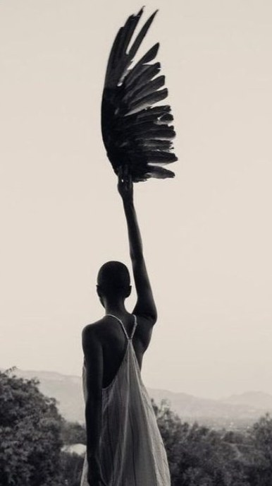 Mulher erguendo uma asa negra contra o céu